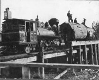 A train engine pushes a large redwood log down railroad tracks. A few men stand on the log.