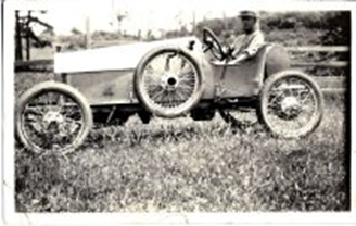 A man sitting in an ancient race car with an extra tire