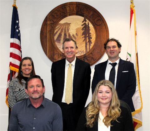 The Board of Supervisors standing in front of the County seal, American flag, and California flag. Pictured left to right are Maureen Mulheren, Bernie Norvell, John Haschak, Madeline Cline, and Ted Williams
